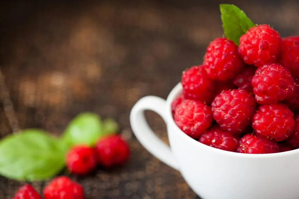 Une tasse remplie de framboises avec quelques framboises dispersées à côté